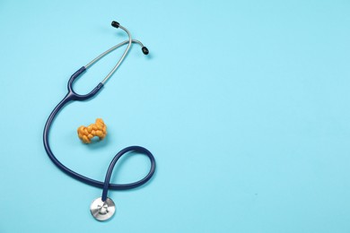 Endocrinology. Stethoscope and model of thyroid gland on light blue background, top view. Space for text