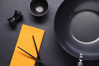 Empty iron wok, sauce bowl and chopsticks on black table, flat lay