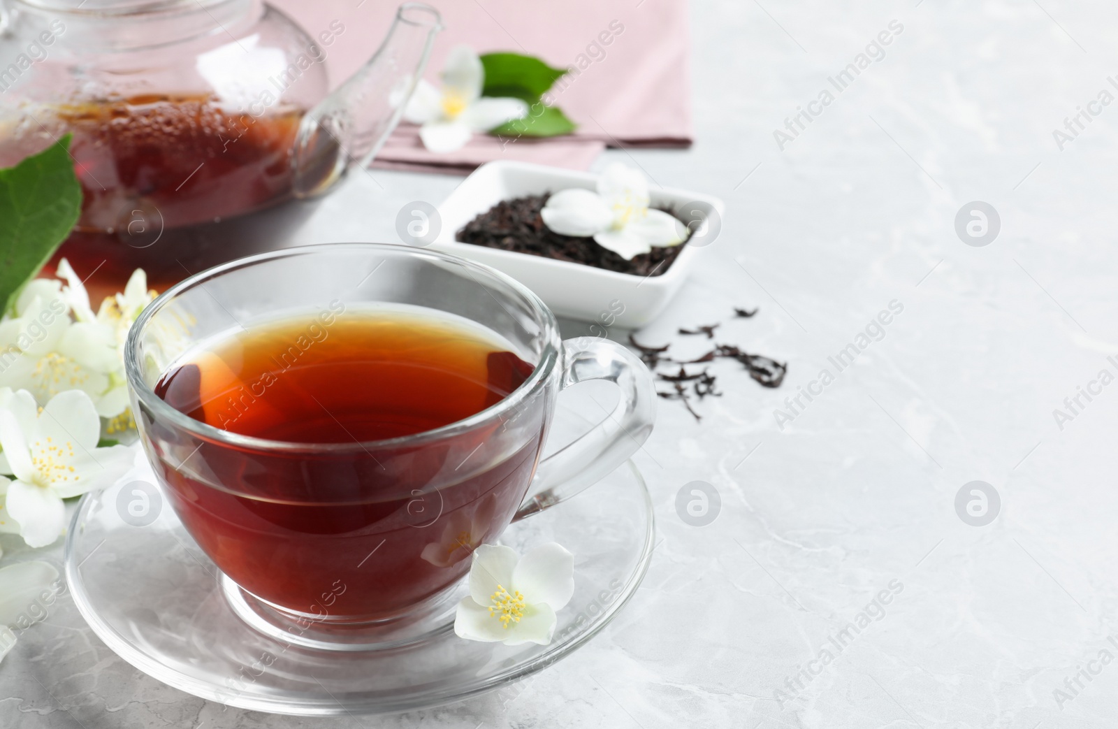 Photo of Cup of tea and fresh jasmine flowers on light grey marble table. Space for text