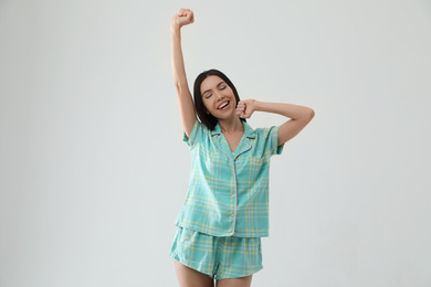 Beautiful Asian woman in pajamas stretching on light grey background. Bedtime