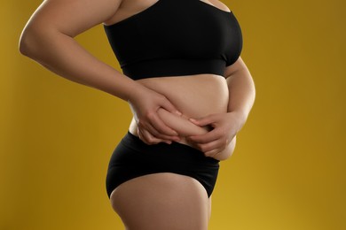 Woman touching belly fat on goldenrod background, closeup. Overweight problem