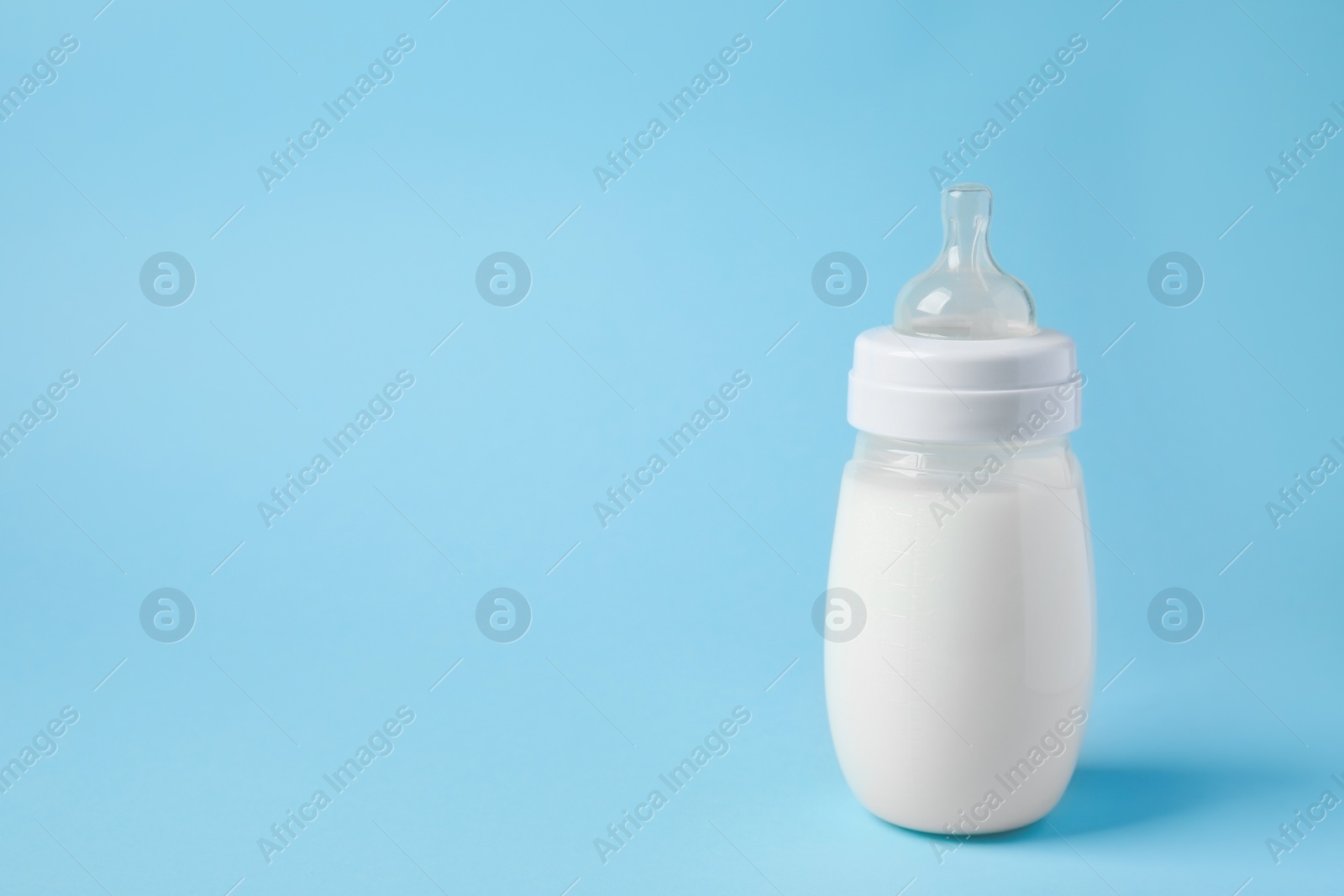 Photo of One feeding bottle with milk on light blue background. Space for text