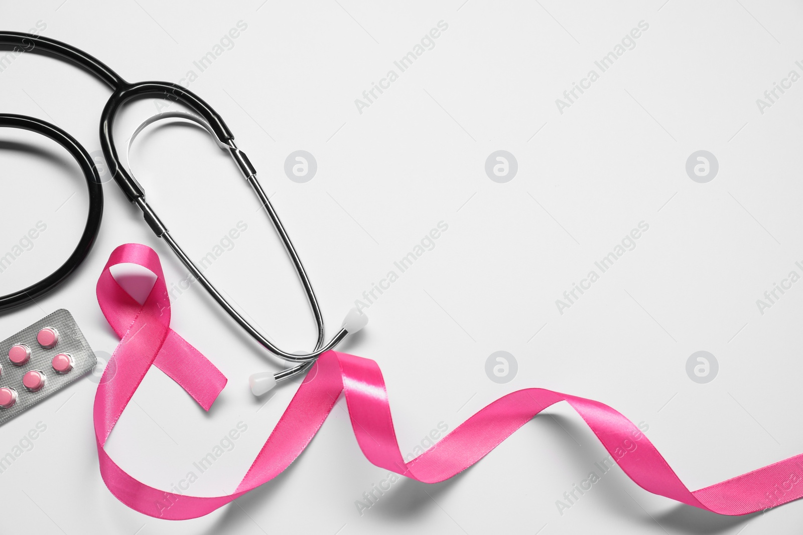 Photo of Breast cancer awareness. Pink ribbon, stethoscope and pills on white background, flat lay. Space for text