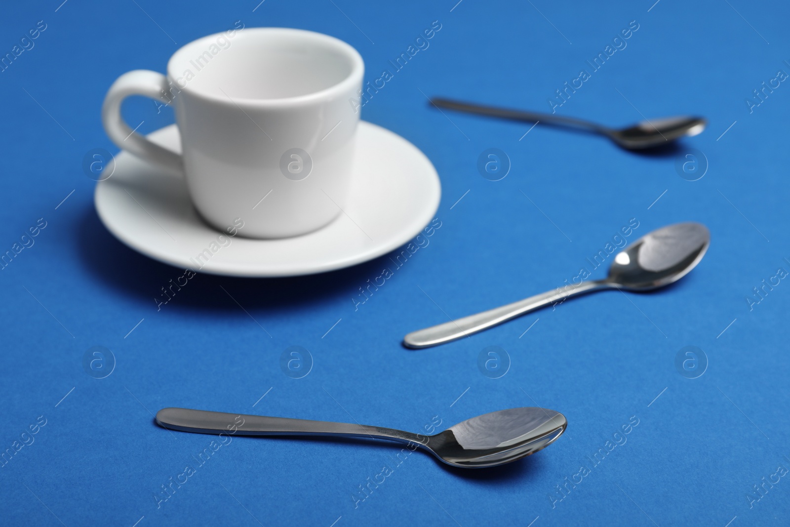 Photo of Teaspoons and cup with saucer on blue background