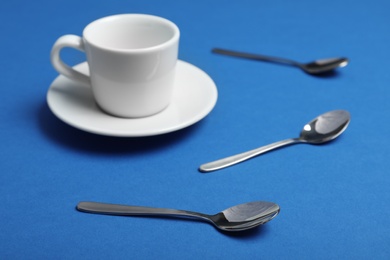 Teaspoons and cup with saucer on blue background