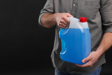 Photo of Man holding canister with blue liquid on black background, closeup. Space for text