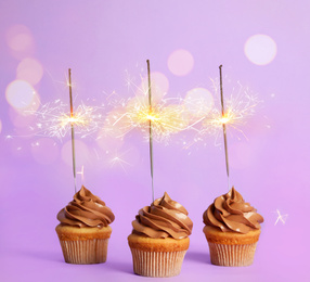 Image of Birthday cupcakes with sparklers on violet background