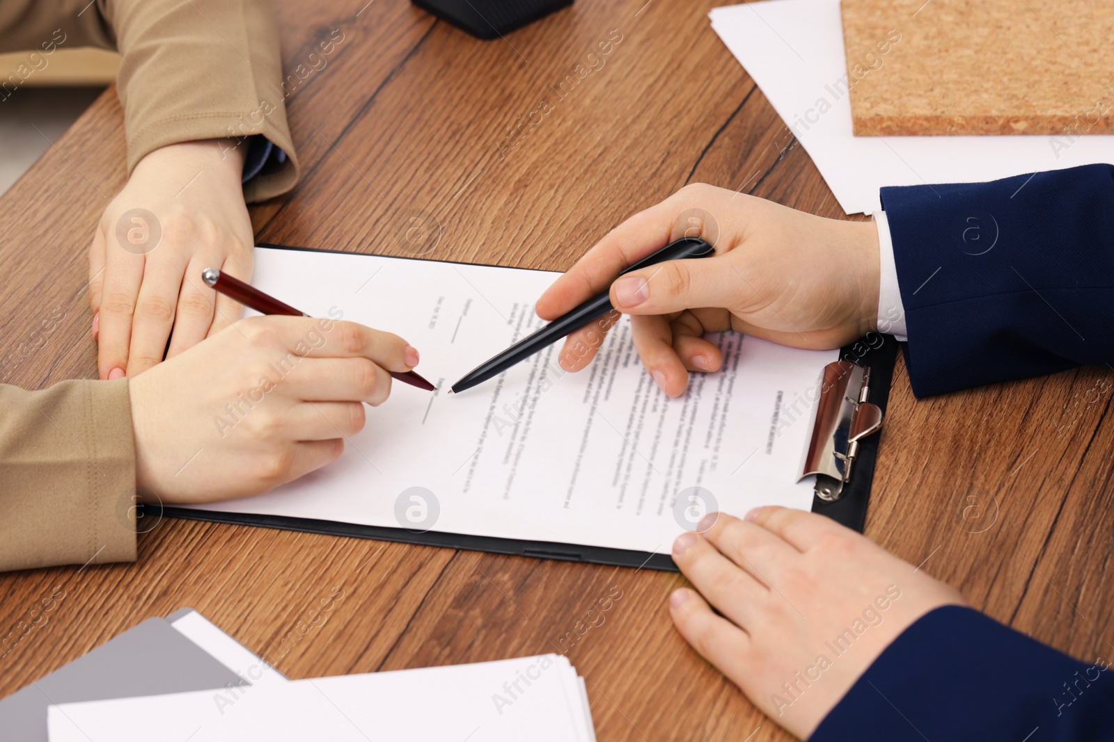 Photo of Man pointing at document and woman putting signature at wooden table, closeup