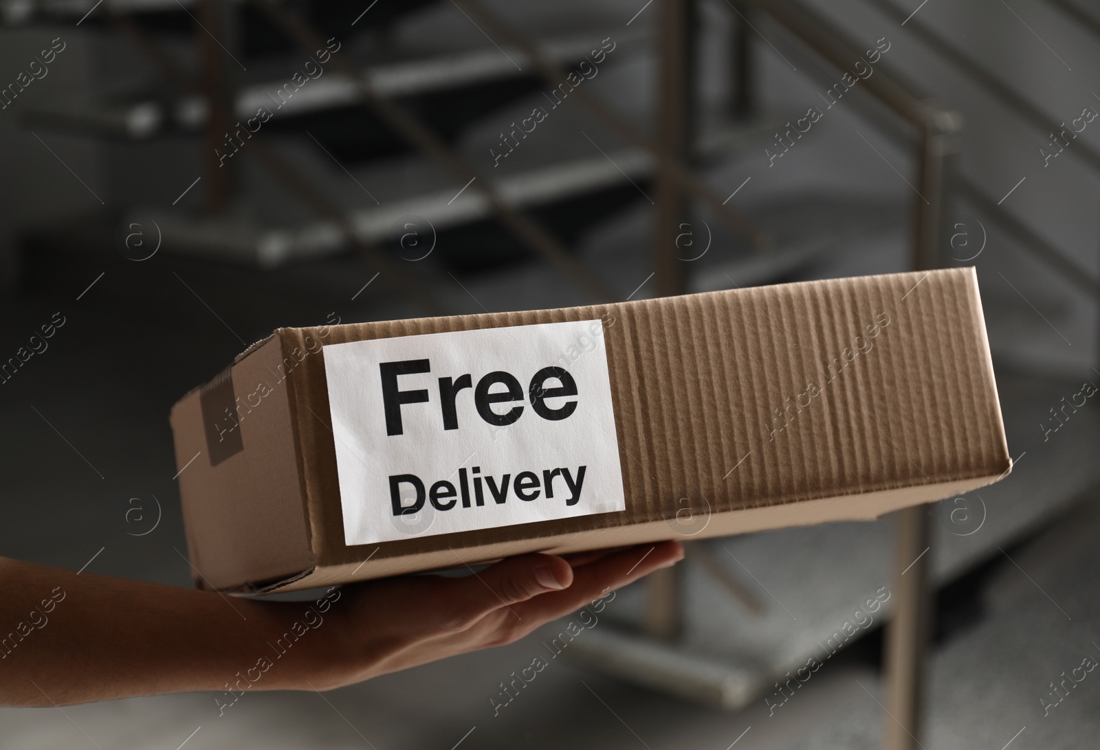 Photo of Courier holding parcel with sticker Free Delivery indoors, closeup