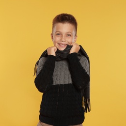 Photo of Cute little boy in warm sweater and scarf on yellow background. Winter season