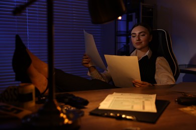 Photo of Professional detective working with documents at table in office at night