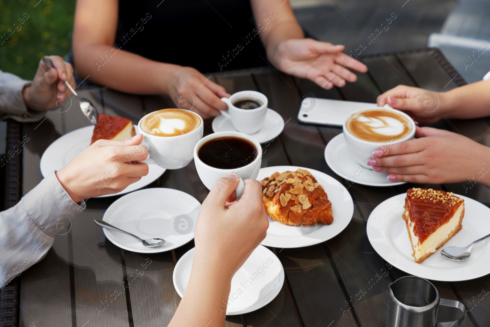 Photo of Friends drinking coffee at wooden table in outdoor cafe, closeup