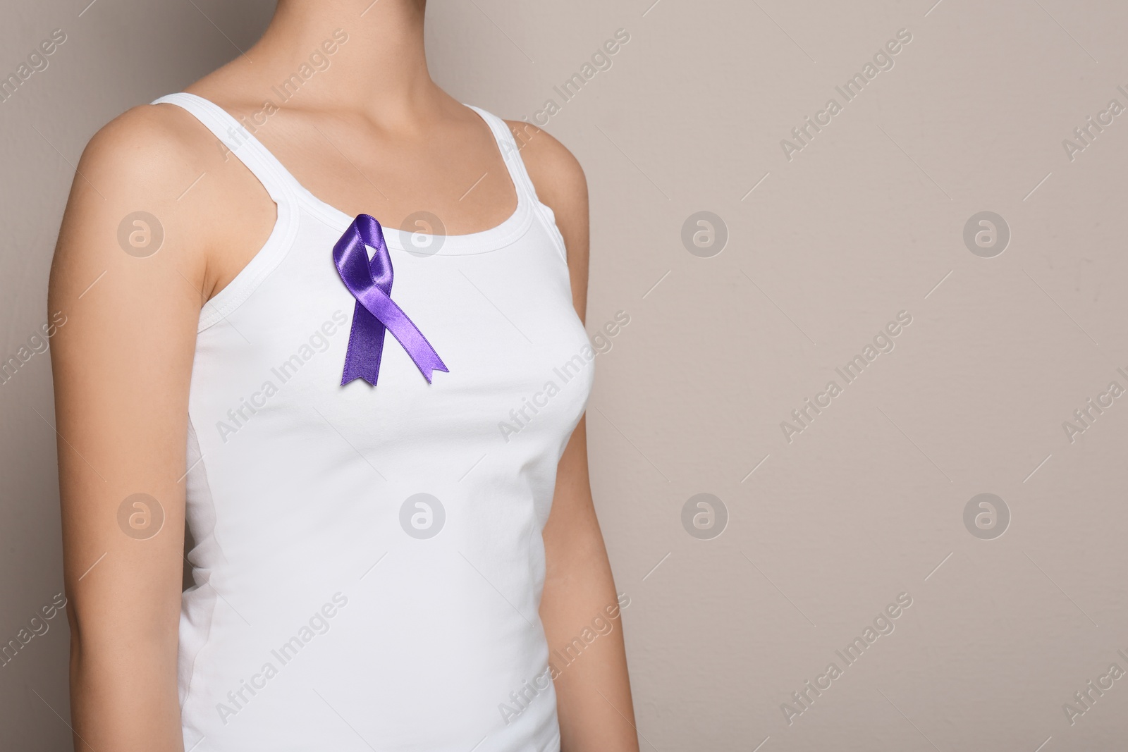 Photo of Woman wearing purple ribbon on grey background, closeup with space for text. Domestic violence awareness