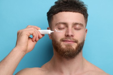 Photo of Handsome man applying moisturizing cream onto his face on light blue background