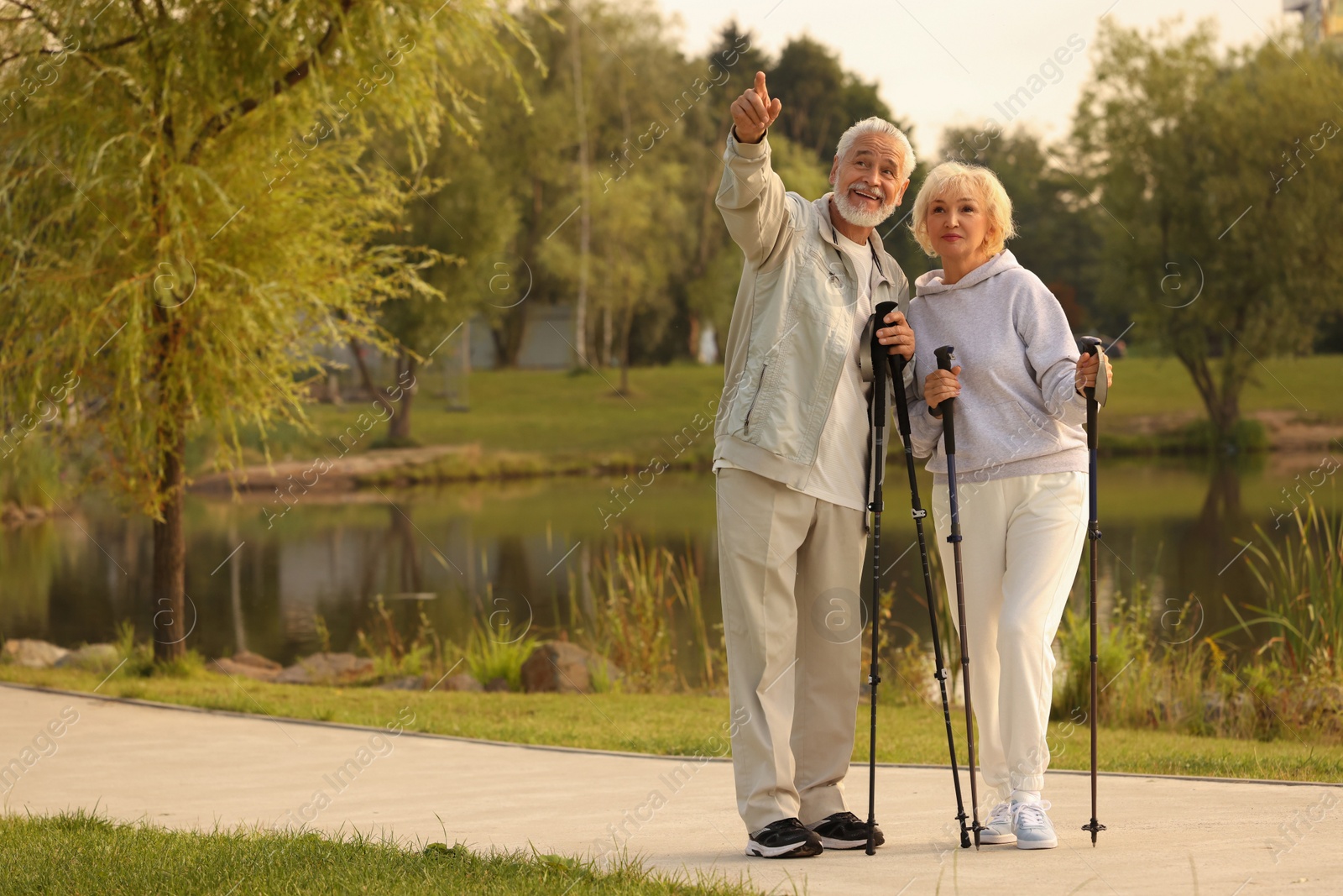 Photo of Senior man and woman with Nordic walking poles outdoors, space for text