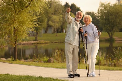 Photo of Senior man and woman with Nordic walking poles outdoors, space for text