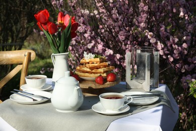 Photo of Beautiful bouquet of tulips and freshly baked waffles on table served for tea drinking in garden