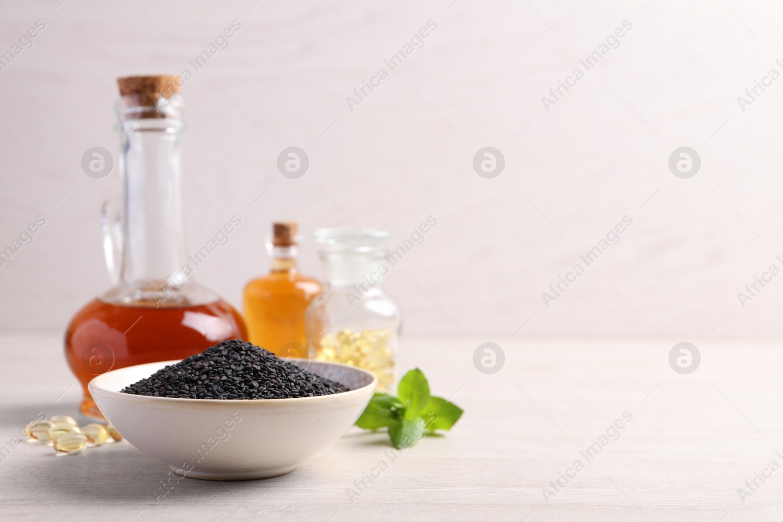 Photo of Black sesame seeds and oil on white wooden table, space for text