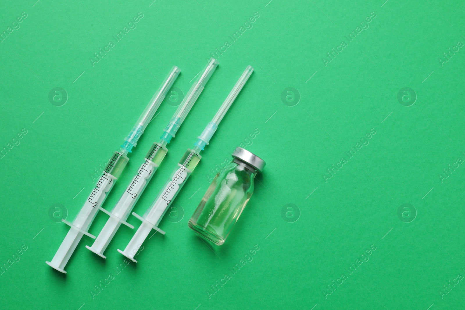 Photo of Disposable syringes with needles and vial on green background, flat lay. Space for text