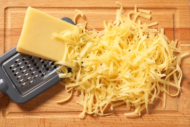 Photo of Grated, whole piece of cheese and grater on wooden board, top view