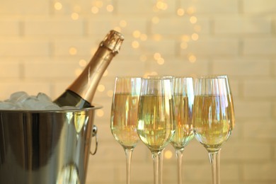 Photo of Glasses of champagne and ice bucket with bottle on blurred background