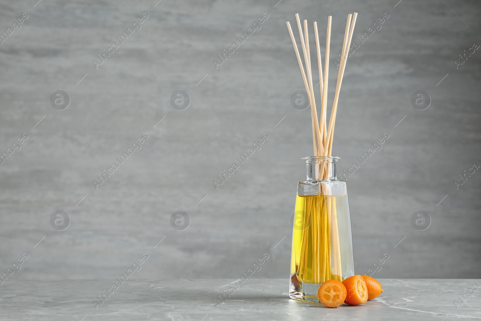 Photo of Aromatic reed freshener and kumquat on table against grey background. Space for text