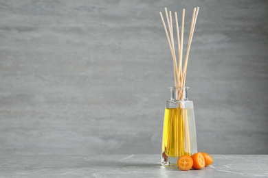 Photo of Aromatic reed freshener and kumquat on table against grey background. Space for text