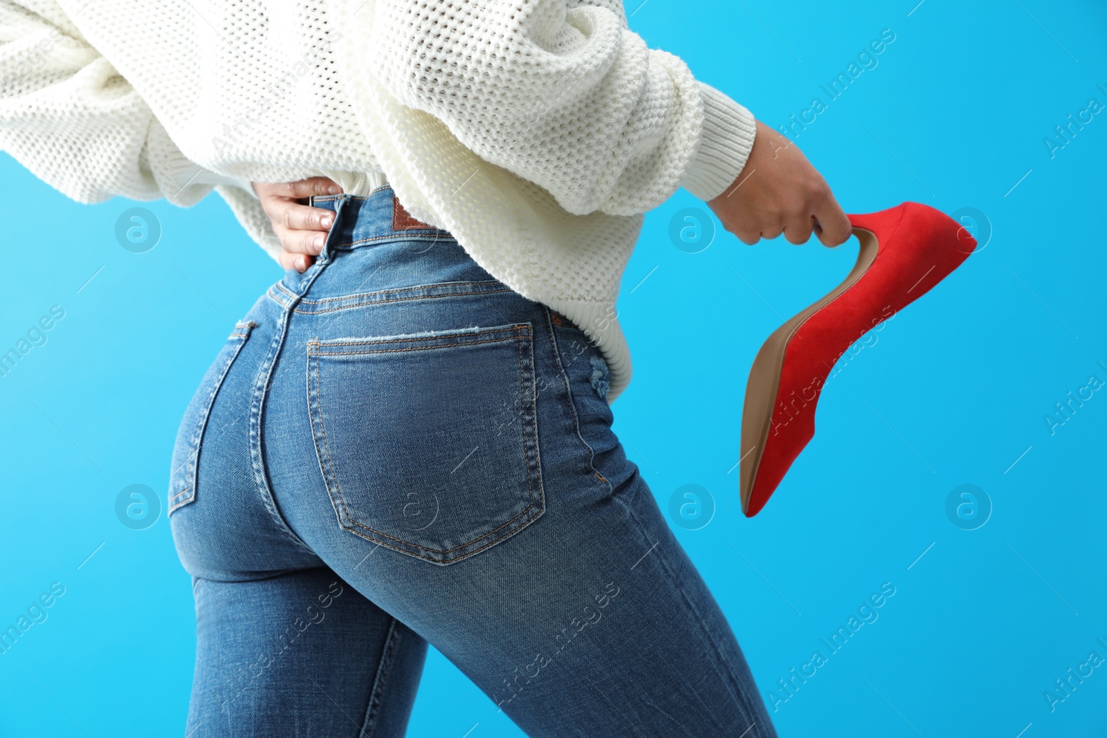 Photo of Woman in jeans holding red shoe on blue background, closeup