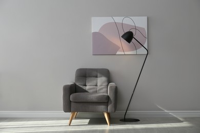 Stylish armchair and lamp near grey wall with beautiful picture. Interior design