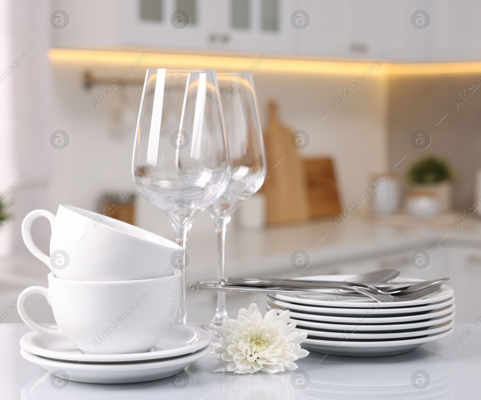 Photo of Set of clean dishware, glasses, cutlery and flower on table in kitchen