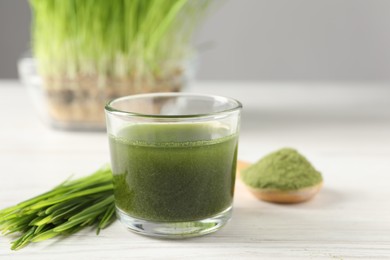 Photo of Wheat grass drink in glass and fresh sprouts on white wooden table, closeup