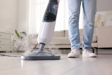 Photo of Man cleaning floor with steam mop at home, closeup