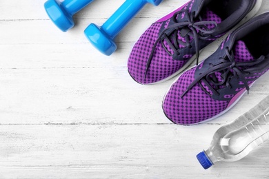 Flat lay composition with dumbbells, sneakers and space for text on wooden background