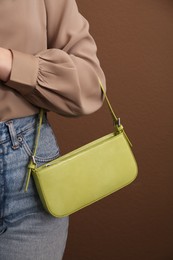 Woman with stylish baguette handbag on brown background, closeup