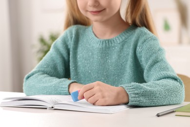 Photo of Girl using eraser at white desk indoors, closeup