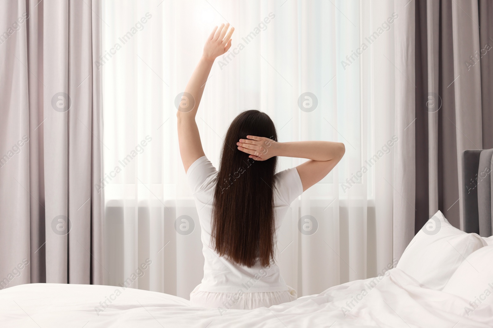 Photo of Woman stretching on bed at home, back view. Lazy morning