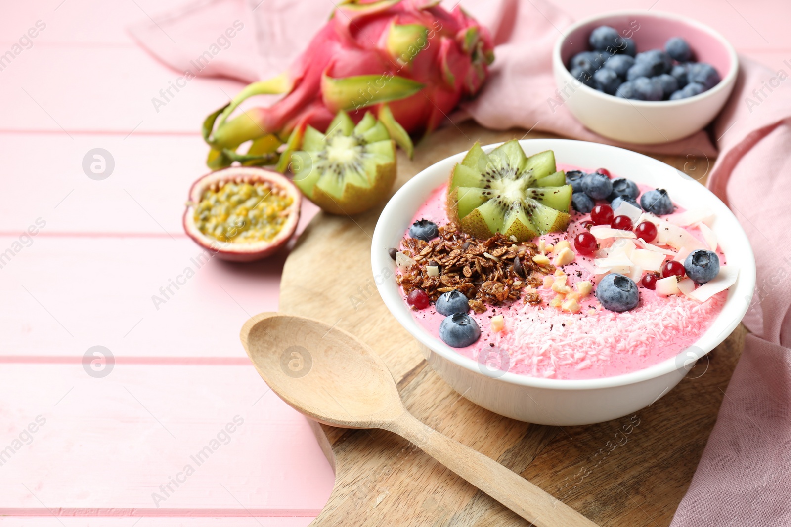 Photo of Tasty smoothie bowl with fresh kiwi fruit, berries and granola on pink wooden table. Space for text