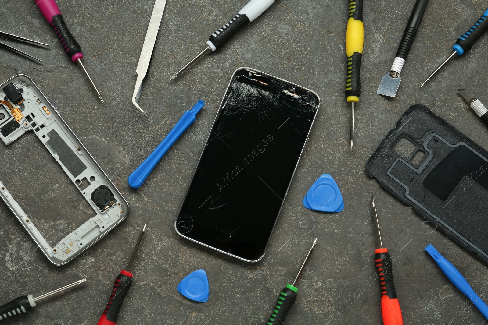 Photo of Parts of damaged smartphone and repair tool set on grey table, flat lay