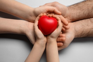 Photo of Parents and kid holding red heart in hands on light grey background, top view