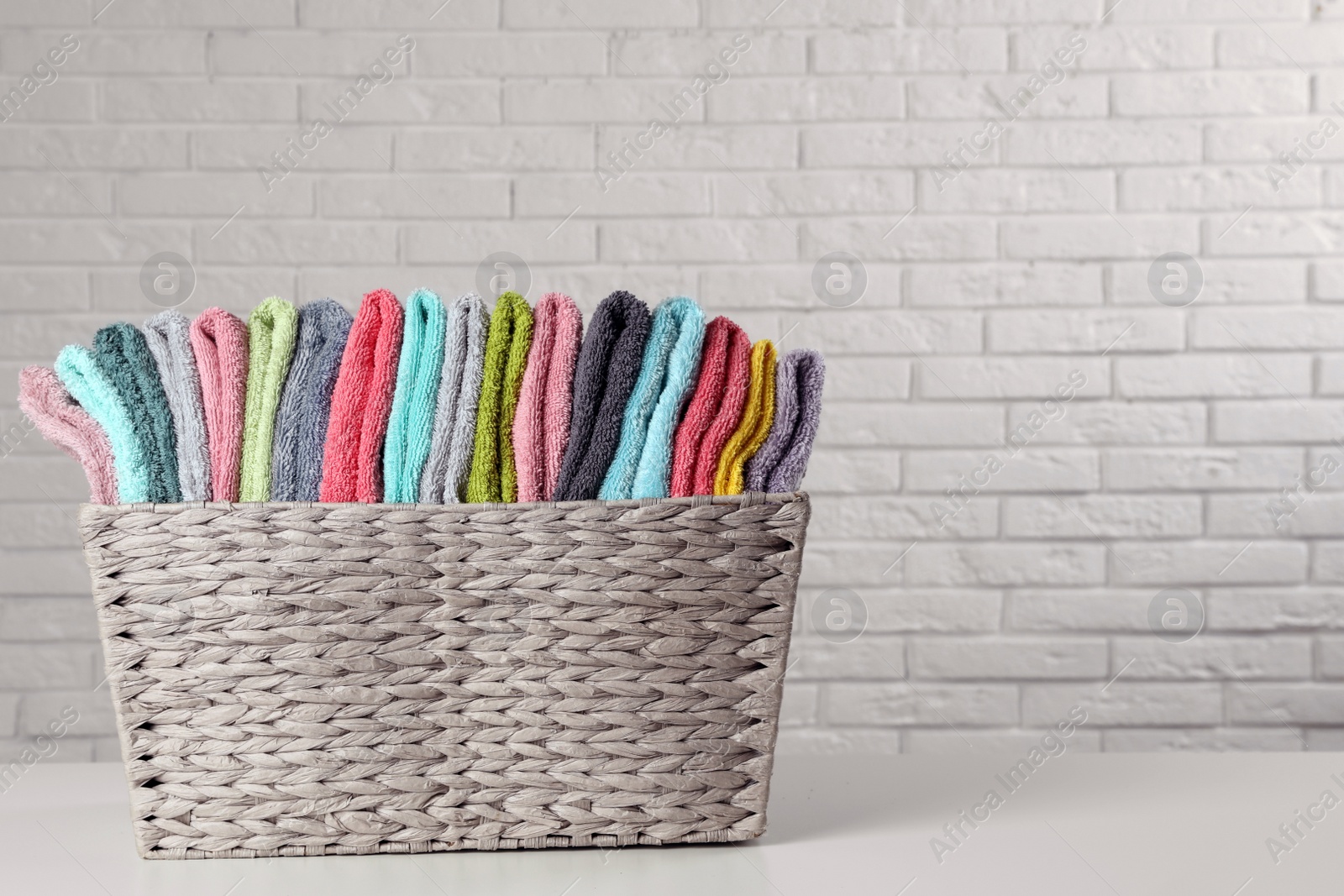 Photo of Wicker basket with folded towels on table near white brick wall. Space for text