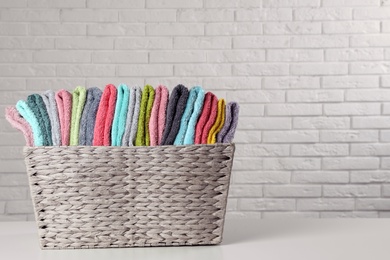 Photo of Wicker basket with folded towels on table near white brick wall. Space for text