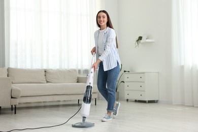 Photo of Happy woman cleaning floor with steam mop at home
