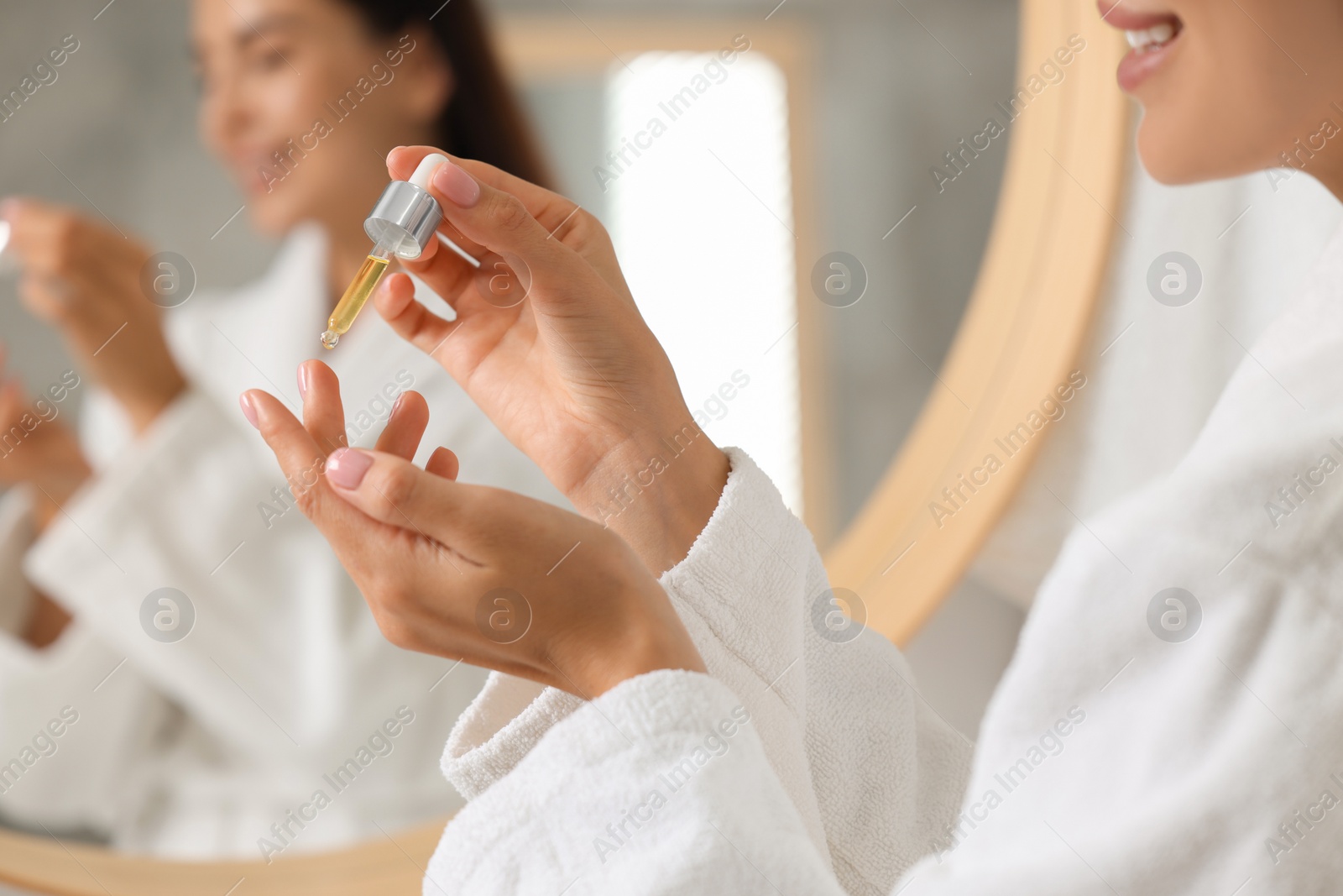 Photo of Young woman applying cosmetic serum onto her hand indoors, closeup