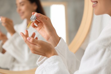 Young woman applying cosmetic serum onto her hand indoors, closeup