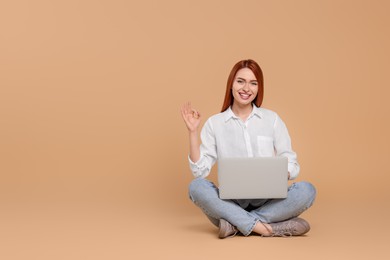Photo of Smiling young woman with laptop showing OK gesture on beige background, space for text