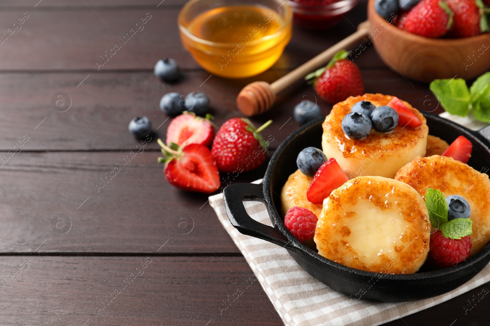 Photo of Delicious cottage cheese pancakes with fresh berries and honey on wooden table, space for text