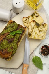 Freshly baked pesto bread with basil served on white table, flat lay