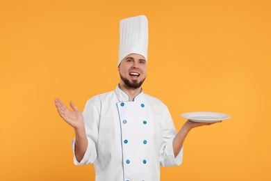 Happy professional confectioner in uniform holding empty plate on yellow background