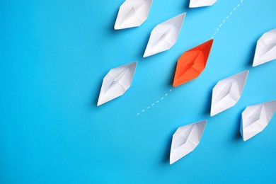 Photo of Orange paper boat floating between others on light blue background, flat lay with space for text. Uniqueness concept
