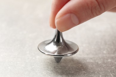 Photo of Woman playing with metal spinning top at grey textured background, closeup
